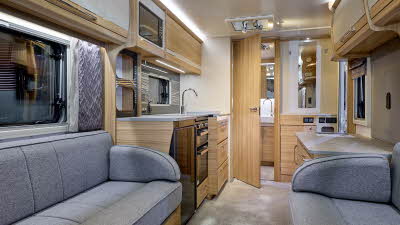 Bailey Unicorn Seville interior, it is grey with light wood.  The kitchen has a full oven and an under the counter fridge.  There is a rear washroom beyond the kitchen and its door is open.  