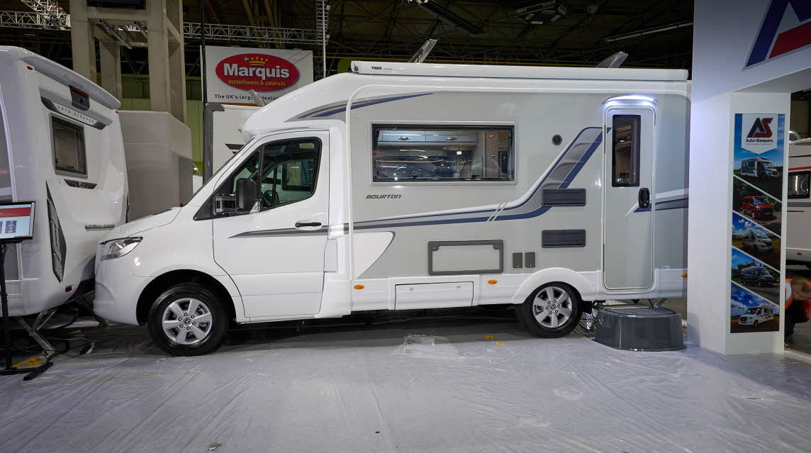 Auto-Sleeper Bourton's exterior has a white cab and grey body with grey/blue decals.  The entrance door is closed and there is a step to gain easy access.