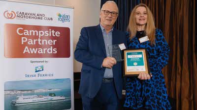 A Caravan and Motorhome Overseas Campsites Award Winner with the Chairman next to a sign showing Campsite Partner Awards, with Irish Ferries below it