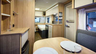 Interior of the Knaus Sport 460 EU with blue and grey sofas, wooden accents and a wooden floor.  The fixed single beds are towards the rear, just past the kitchen.