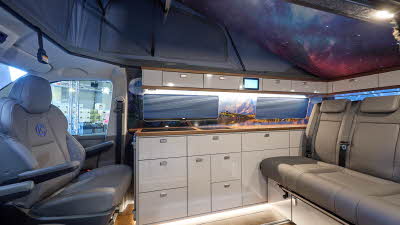 Knights Prestige Plus' interior has grey upholstery.  The furniture is white with a wooden surround.  The roof is extended and there is screen featuring the solar system.