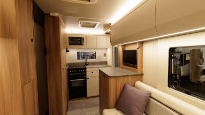 The Auto-Trail Imala 615 has cream upholstery and wooden furniture.  The kitchen is to the rear and there is a domestic style oven with a microwave in a cupboard above it.