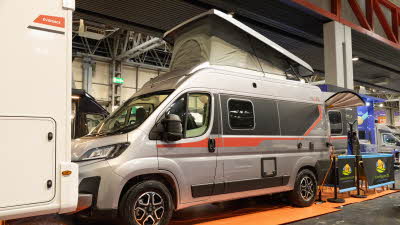 The Pilote V540G has a grey exterior with a red striped decal.  Its rising roof is open and it is plugged into the mains electricity