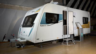Xplore 585's exterior is white with turquoise and gold graphics, the door is open and there's a metal step for easy access into the interior.