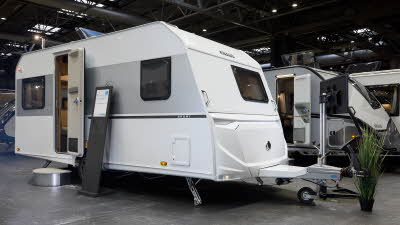 Knaus Sport 450 FU’s exterior is white with a grey decal stripe.  At the front there is a small window.  The entrance door is open with a step to gain easy access.  There is an information board to the right of the door.  Its roof light is open.