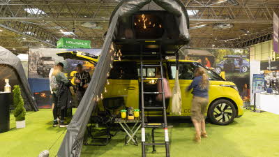 The Roof Space 2 has black and grey canvas.  Its door is open and it has a fitted annex.  There is a black ladder to gain entry.  It is displayed on a yellow MPV.