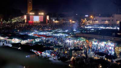 the busy main souk of Marrakech at night, with the stalls lit up brightly