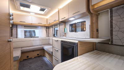 Knaus Sport 450 FU's interior is cream and wooden.  There is a u shaped sofa at the front.  The fixed bed is at the front of the picture.  There is a worktop extension over the bed.