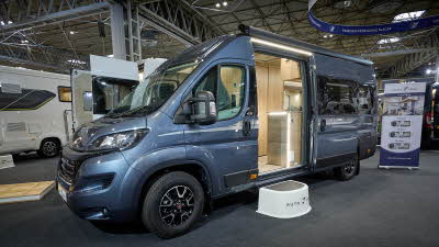 Auto-Trail V-Line 635 Sport's exterior is mid grey with silver decals.  The sliding door is open revealing the kitchen and there is a white step to gain easy access.  There is a roller banner to the rear.
