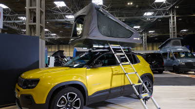 The TentBox GO is shown on a yellow jeep.  Its canvas is grey with black windows.  There is a silver ladder.