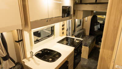 The Elddis Autoquest APEX 196+'s kitchen has a square sink next to the oven.  There is a microwave in a cupboard above the hob.  The drop down bed is in its travelling position.