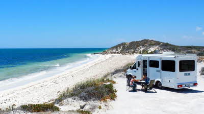 Relaxing beside a motorhome parked above the sand dunes facing a beautiful sandy beach and the ocean