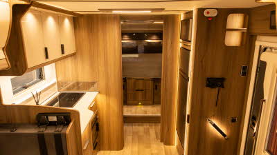 The Coachman Travel Master 545 has a interior primarily made from wood.  The kitchen is on the left and there is a separate rear bed.  The cabinets are cream.