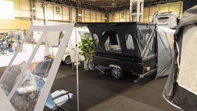 The Campmaster One Motion Comfort has a black unit with a large grey annex at its back.  The front has a canopy with two blue chairs