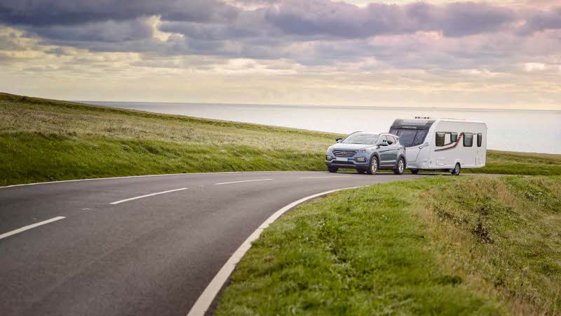 Car towing caravan driving down road surrounded by peaceful scenery