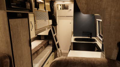 The WildAx Motorhomes Solaris XL has brown and cream upholstery with matching cabinets.  There are two bunk beds to the rear opposite the kitchen.  