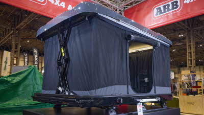 The ARB 4x4 Accessories Altitude is fully extended with two crossed mechanical poles.  It has a solid grey roof and the sides are made of grey canvas.  The door is open, revealing a pocket and a closed window. 
