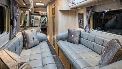 Auto-Sleeper M-Star's interior has grey leather upholstery.  There are four beige cushions with the Auto-Sleeper logo.  It has pale wooden furniture with grey inserts on the overhead lockers.   