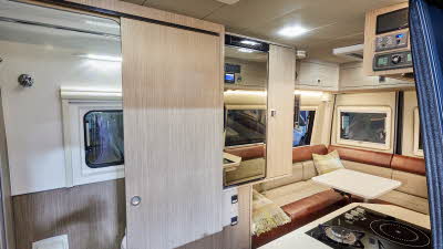 RP Motorhomes Rebel AWD U has two tone copper and cream upholstery.  There are wooden overhead lockers. There is a wooden sliding door to the washroom.  There is a hob with two gas rings and an addition there is an induction plate 
