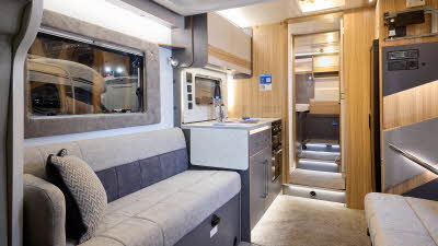 The Bailey Adamo XL T has beige carpets, with cream and pale wood cabinets.  The upholstery is cream and dark brown.  There are three steps up to the fixed rear bed.  
