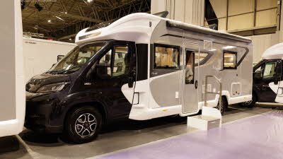 The Bailey Autograph 79-4F has a black cab and a white/grey coachbuilt body.  There is a silver step outside the habitation door.  The two skylights are open.