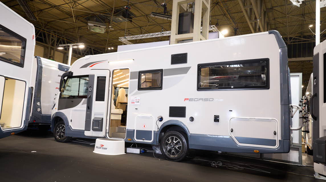 The Roller Team Pegaso 745 is white with blue trim and grey and red decals.  There is a white step outside the open habitation door. 