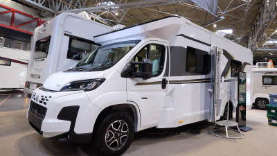 The Elddis Avalon 285 has a white body with black and gold decals.  There is a metal step by the open habitation door, there is an interactive stand to the right.