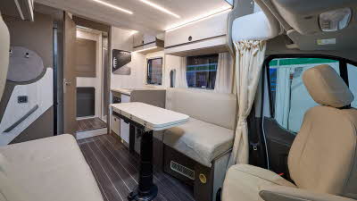 Rimor Kilig 67 Plus’ interior has cream upholstery.  Its furniture is dark wood with cream doors.  It has a wood effect floor.  The lounge’s table is folded and can be extended.  There is a tied up cream curtain which can shut off the front window.