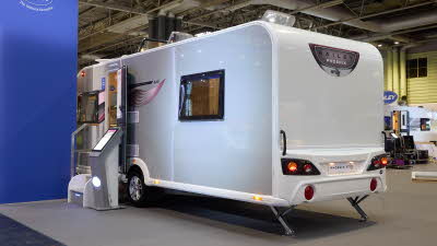 Bailey Phoenix GT75 640's exterior is grey with a purple patterned decal from the front to the rear window.  The entrance door is open and there are two metal steps to gain easy access.  There is an interactive display board to the right