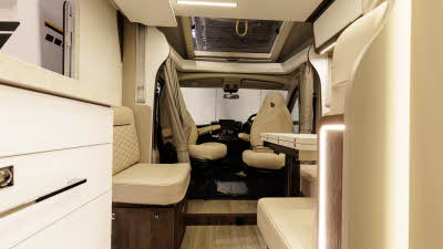 The Benimar Primero 282 has cream upholstery.  The front seats are swivelled to join the lounge.  There is a curtain to separate the cab area in the evening.  There is a white table which can be extended, it's folded.  The sunroof is open.