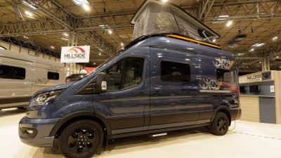 The WildAx Motorhomes Equinox 2WD is blue with yellow and white decals.  Its rising roof is up.