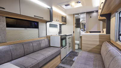 Interior of the Bailey Phoenix Black 420 with grey sofas and wood accents, large windows and two skylights will let natural light flood in.  To the rear the washroom door is open.  