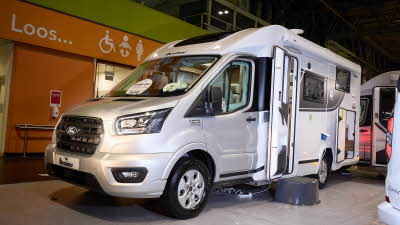 The Benimar Tessoro T861 has a silver cab with a white body.  There is a black step by the open habitation door.  The rear garage door is open. 