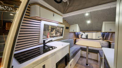 Going Go Pod Flex's interior has cream furniture with grey upholstery.  The walls are covered in slatted wood.  The kitchen is to the right of the entrance door.