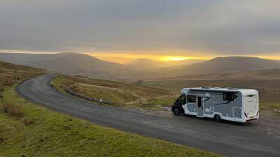 a motorhome parked beside the empty road as the sun sets over the Yorkshire Dales