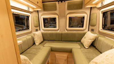 The Vantage TEO has green upholstery and a u shaped sofa.  It has pale wood cabinets.  There is a cream cushion in each corner of the sofa.