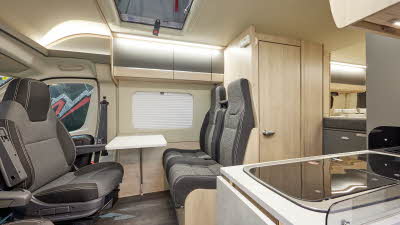 Auto-Trail Expedition 68 has two tone upholstery, with pale wooden furniture.  A hob with extendible flap for additional kitchen work surface is in the kitchen.  The rising roof is open.  The floor is dark wood in colour.