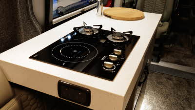 The Hillside Leisure Hopton 600RL has a dual fuel hob with two gas rings and an induction ring.  There is a wooden chopping board style cover over the sink.  There is a double 230V power socket at the front.