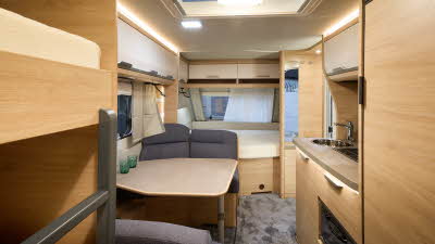 Knaus Südwind 580 QS’s interior has wooden furniture with cream doors, the upholstery is a dark grey.  There are bunk beds to the right and there’s a fixed transverse bed at the front 