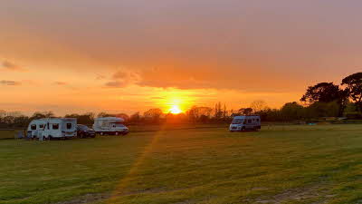 Sun setting over open field with three motorhomes pitched