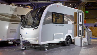 The Bailey Phoenix Black 420 has a grey exterior and a brown decal with light ripples on it.  The entrance door is open and there are two metal steps to gain easy access to the interior.  Next to the steps is an interactive stand.