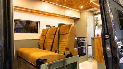 Out and About Campers Summit has mustard coloured upholstery.  There are wooden and green cabinets with a tambour door.  There is a full oven.