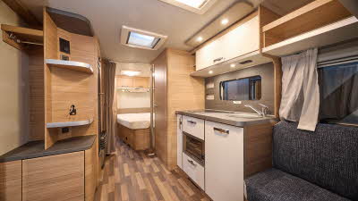 Weinsberg CaraOne 550 UK's interior is primarily wooden with dark grey upholstery.  There is a fixed bed at the rear.  The flooring is two tone wood.
