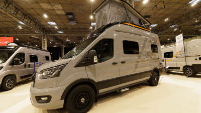 The WildAx Motorhomes Equinox 4x4 is pale grey with black and orange decals.  Its rising roof is fully open.