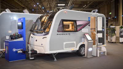 Bailey Phoenix GT75 420's exterior is grey with a purple patterned decal from the front to the rear.  The entrance door is open and there are two metal steps to gain easy access.  There is an interactive display board to the left