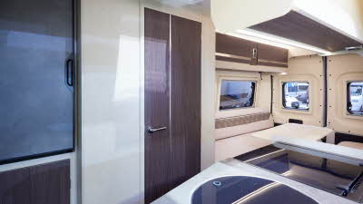 Rimor Horus 66 has two tone cream and patterned upholstery.  The doors are a dark wood.  Towards the rear is a rear lounge.