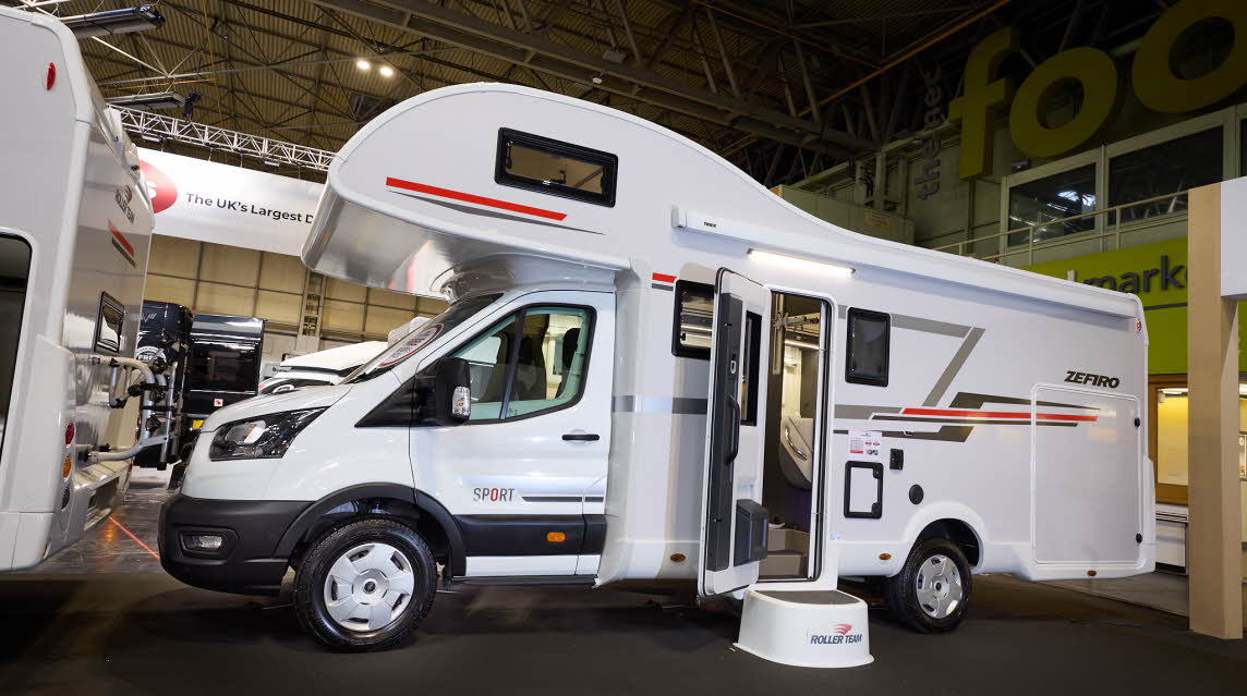 The Roller Team Zefiro Sport has a white cab and its body is white with grey and red decals.  There is a white step outside the open habitation door revealing the interior.