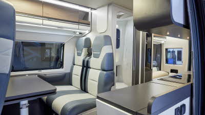 Swift Carrera 184 has blue and white upholstery, the overhead lockers are wooden and white.  The washroom is central; the door is open showing the toilet. To the rear there is a lounge. 