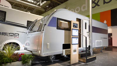 The Adria Alpina Mississippi has a silver exterior with a blue decal that turns to purple at the rear, its entrance door is open and there are two wooden steps to gain easy access. 