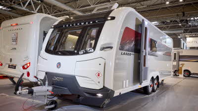 The Coachman Laser 855 Xtra has a white exterior with a red and grey patterned decal.  Its sunroof is open.  The entrance door is open.